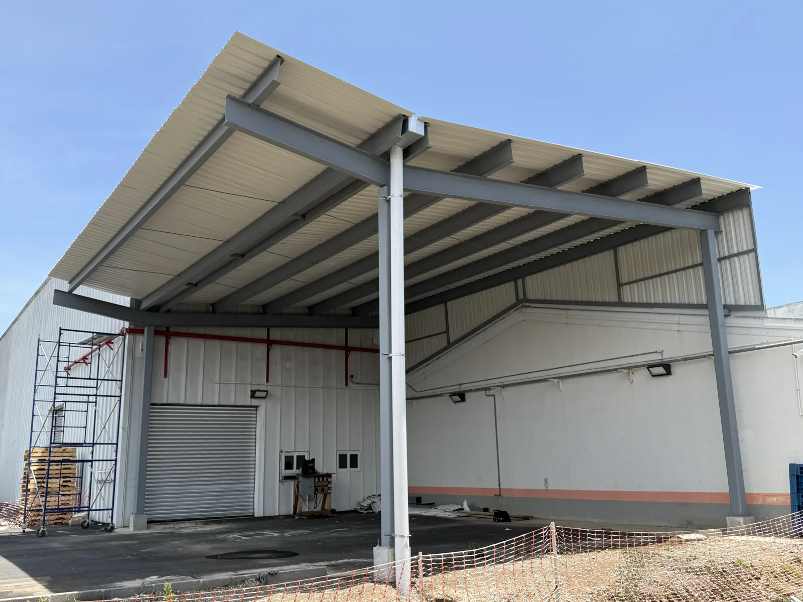 Ampliación con estructura de acero y cubierta metálica junto a una bodega industrial.